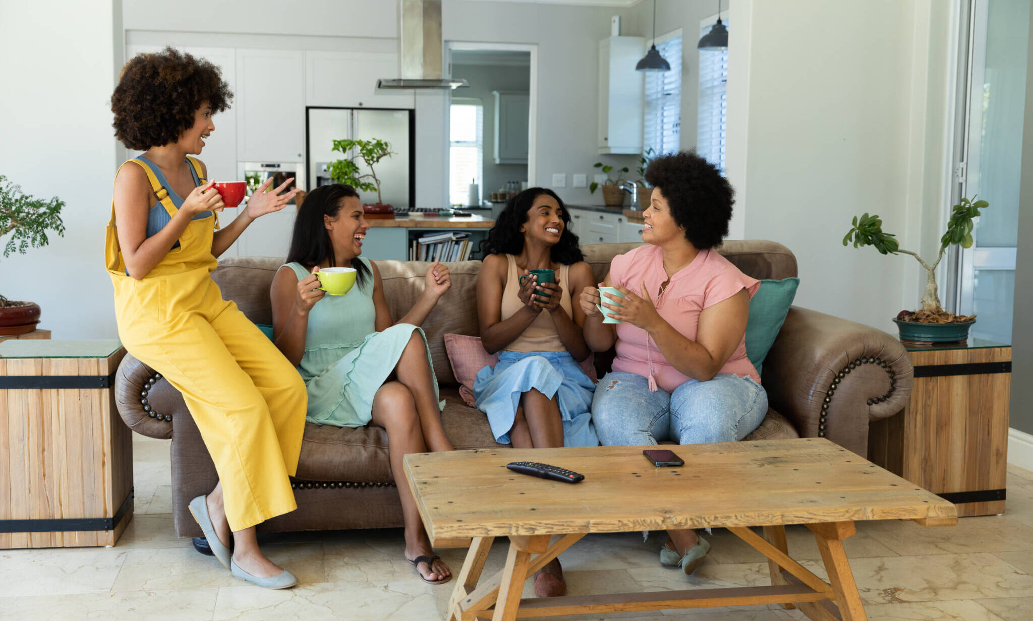 Happy Biracial Female Friends Gossiping And Having Coffee While Sitting On Sofa In Living Room Happy Biracial Female Friends Gossiping And Having Coffee While Sitting On Sofa In Living Room