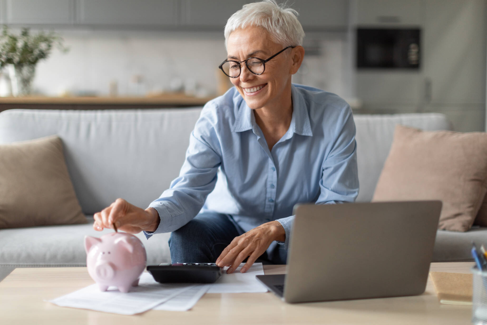 Woman With Piggybank Putting Coin Managing Funds Near Laptop Indoor